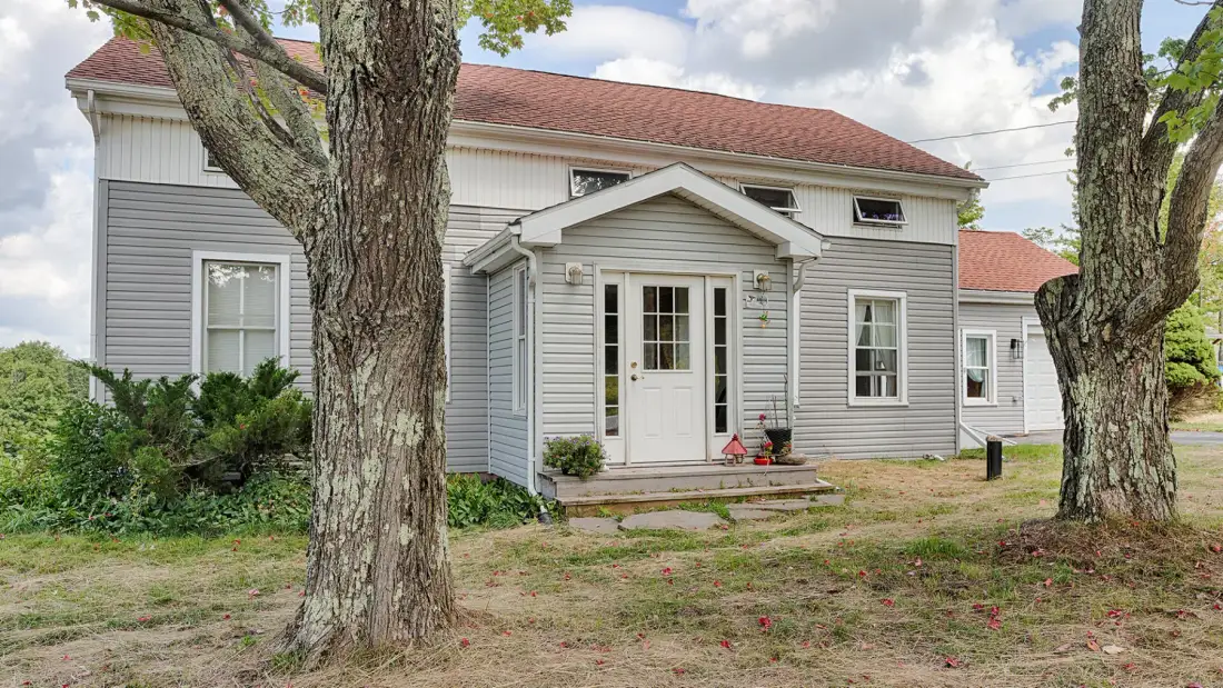 A gray house with white trim stands among trees in a grassy yard.