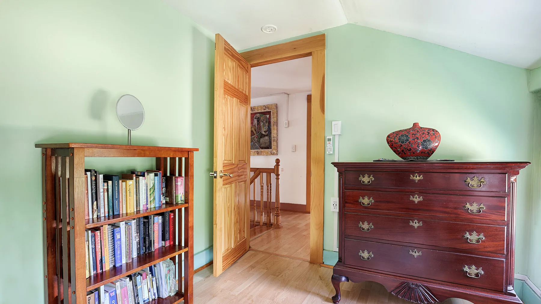 A mint-green bedroom features a wooden bookcase and a dark red dresser.