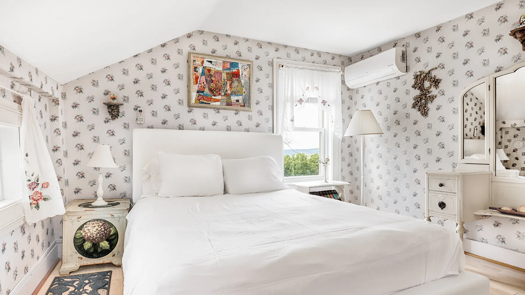 A bedroom with a large bed, floral wallpaper, and windows.