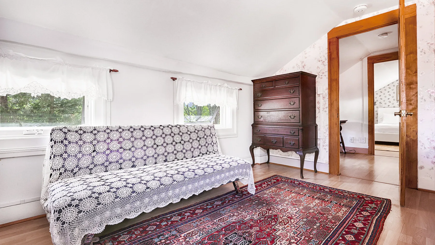 A bright sitting room has a patterned daybed beside a dark wooden chest.