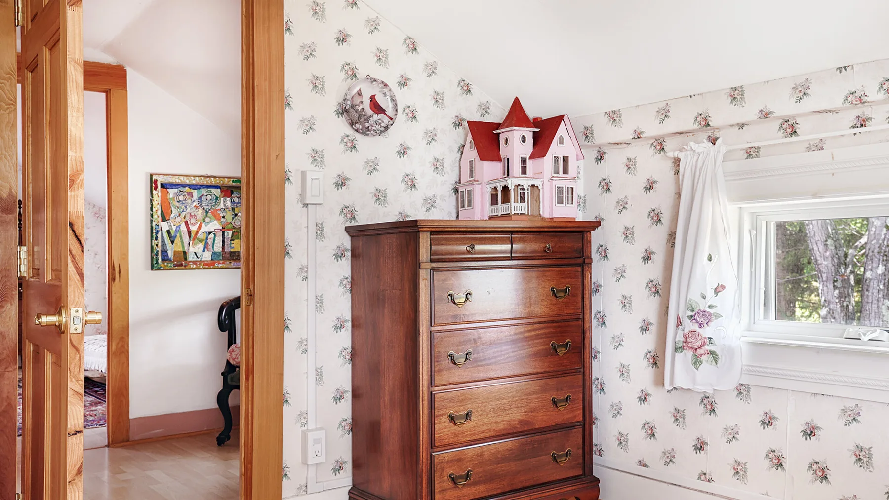 A bedroom with a wooden dresser topped by a toy house and a window.
