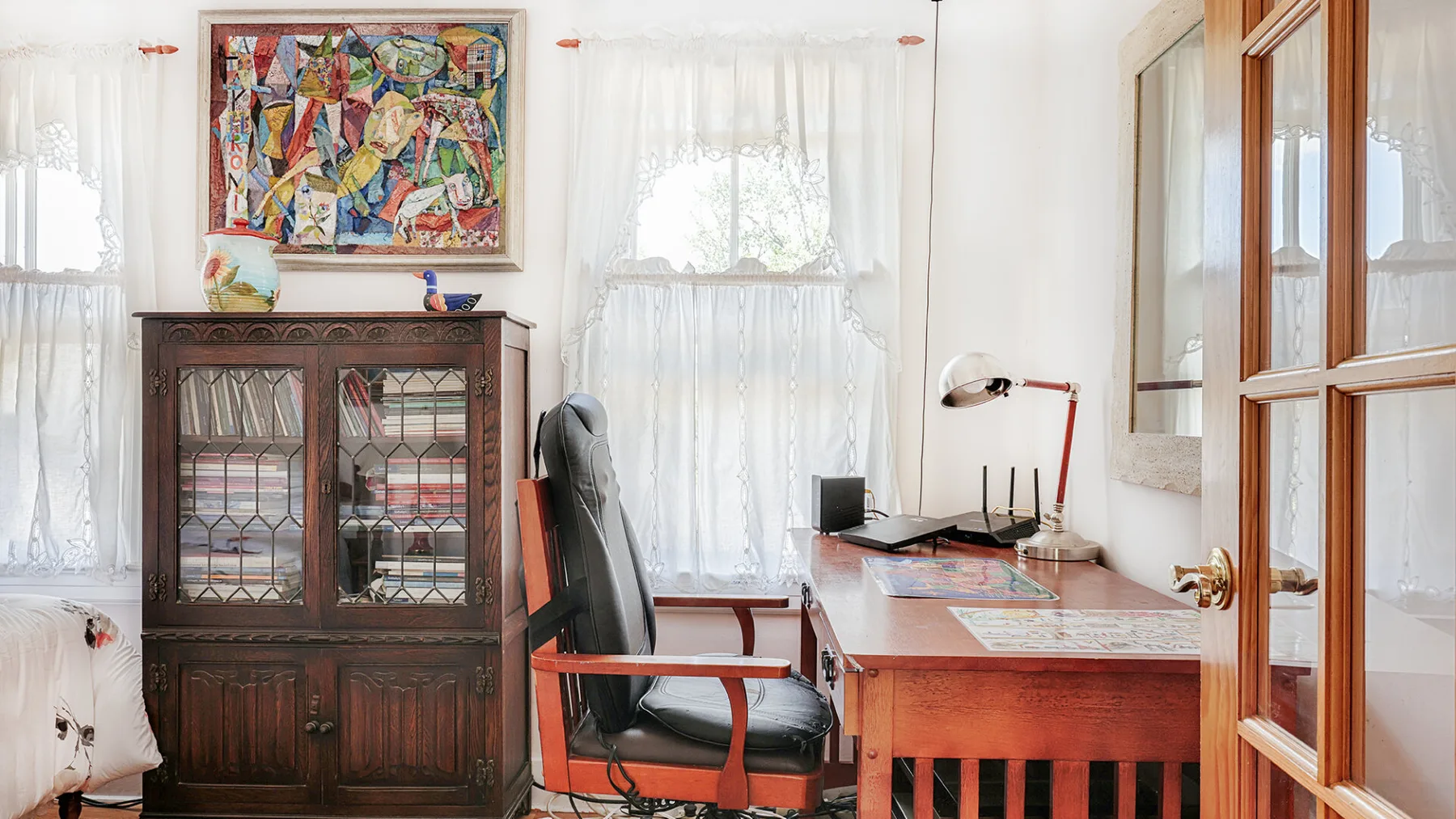 A bright room with a wooden desk, office chair, and glass-front cabinet.