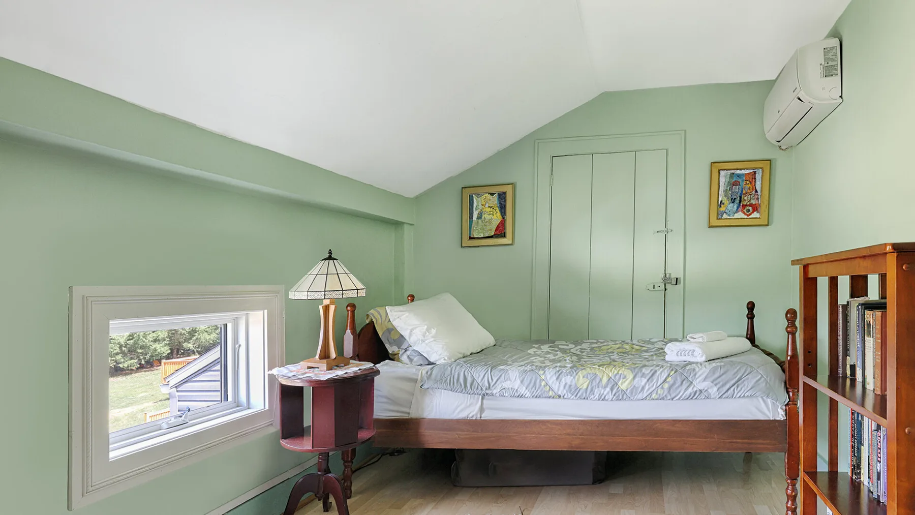 A bedroom with a bed, a window, and a bookcase.