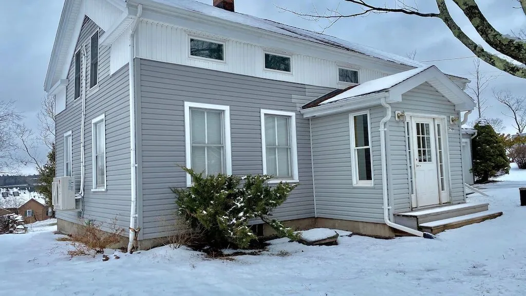A gray-sided house stands in a snow-covered yard.