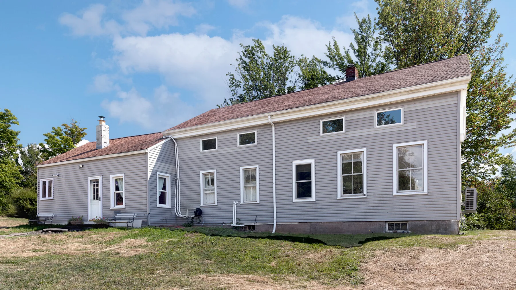 A gray house stands beside a grassy yard under a clear sky.