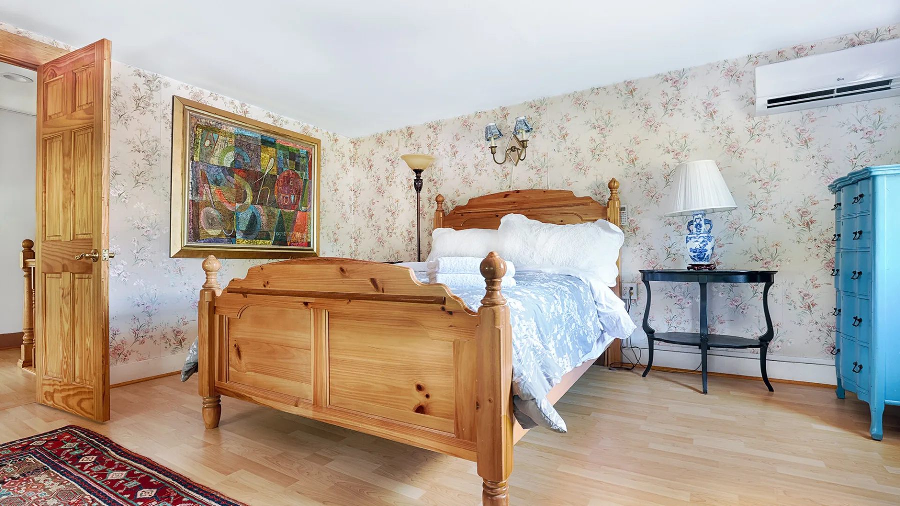 A bedroom with a wooden bed, floral wallpaper, and framed artwork.