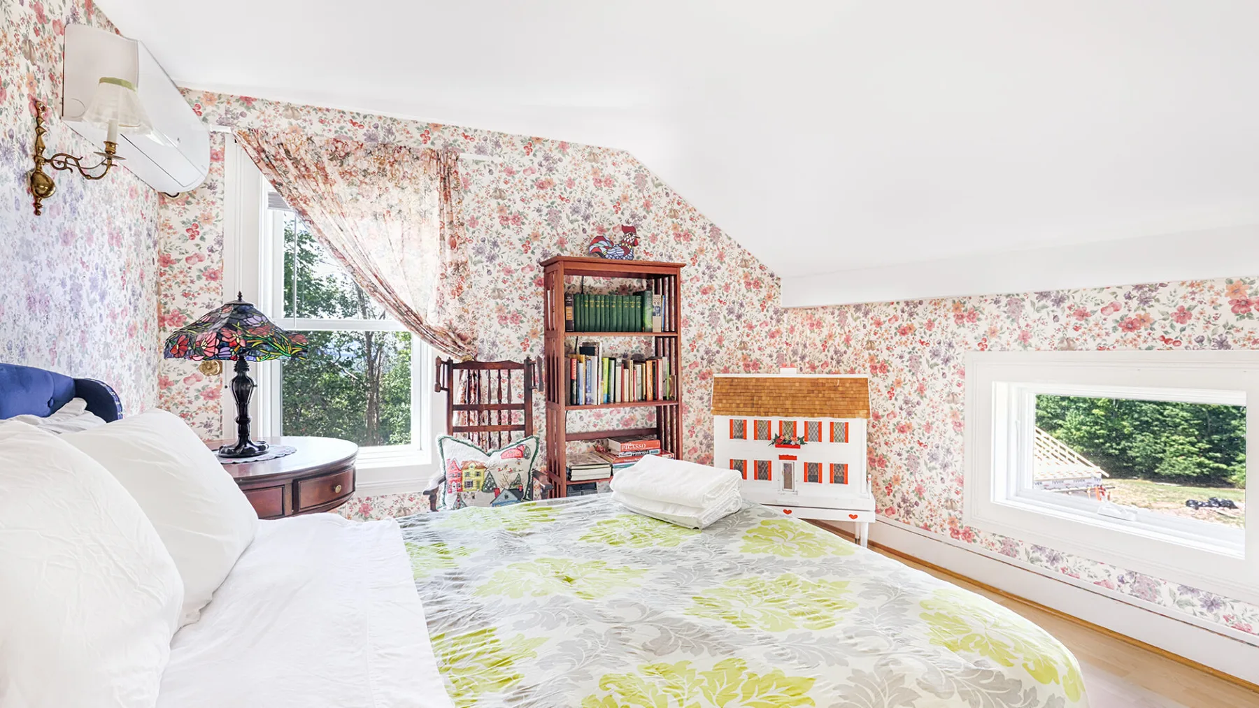 A bright bedroom with floral wallpaper, a bed, and large windows.
