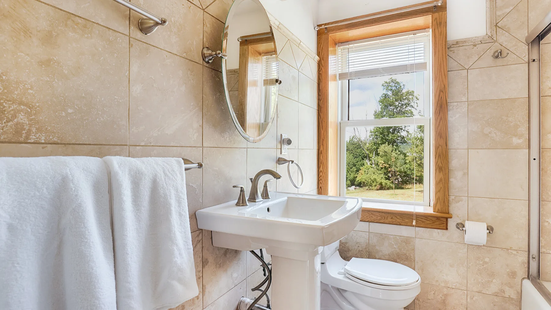 A bright bathroom with a sink, mirror, and window overlooking greenery.