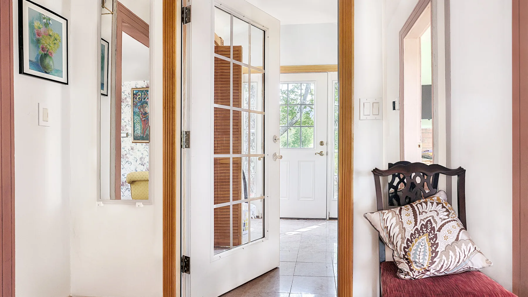 A bright hallway opens to a white entry door, with a small seating nook beside it.
