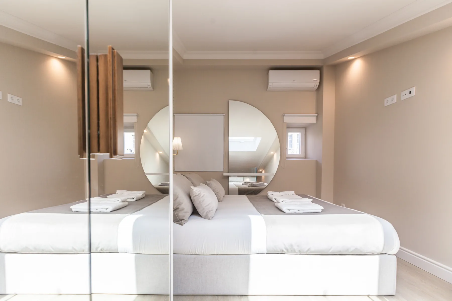 A bright bedroom with a neatly made bed and mirrored wall panels.