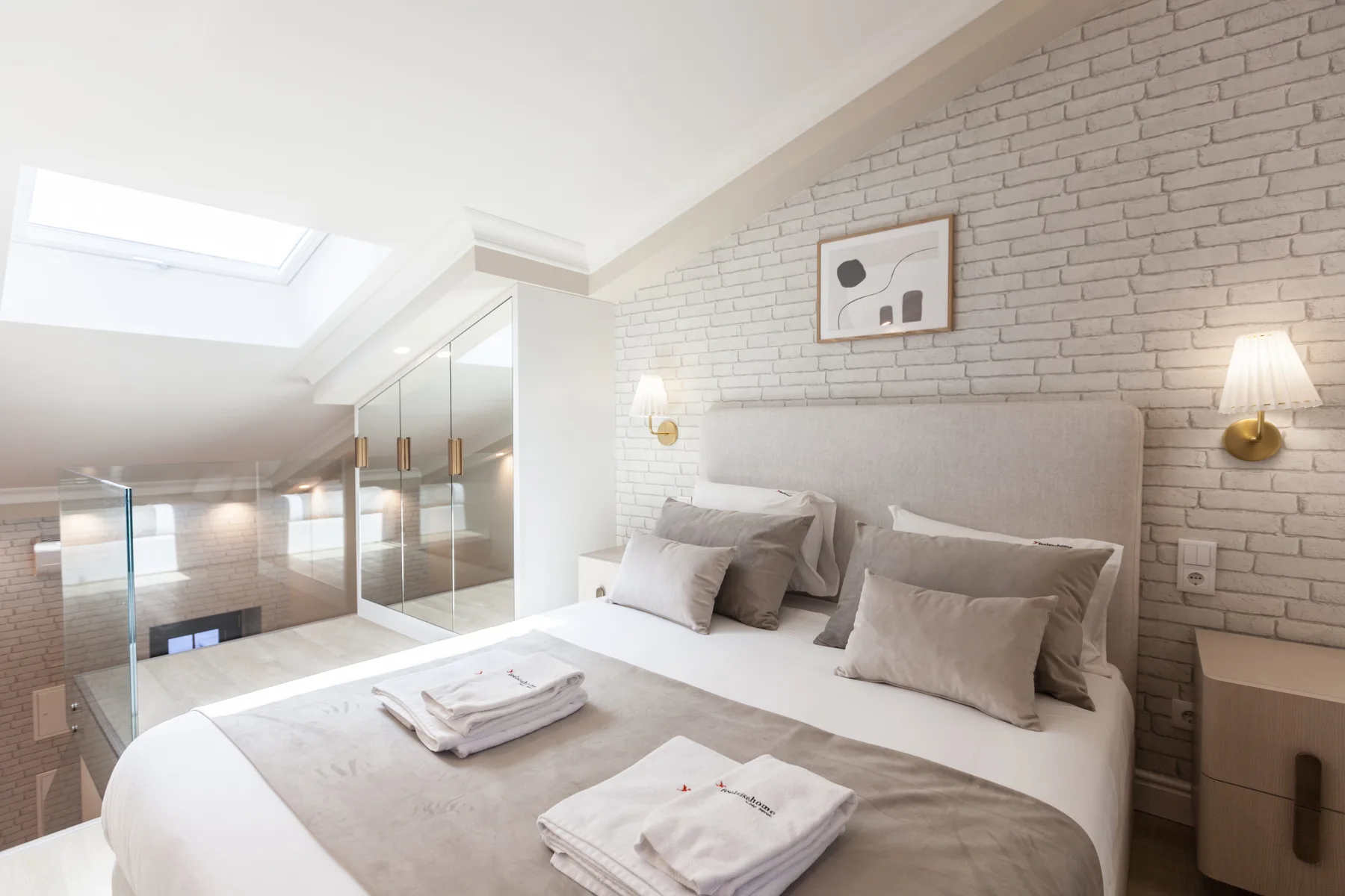 A bright bedroom features a large bed beneath a white brick wall.