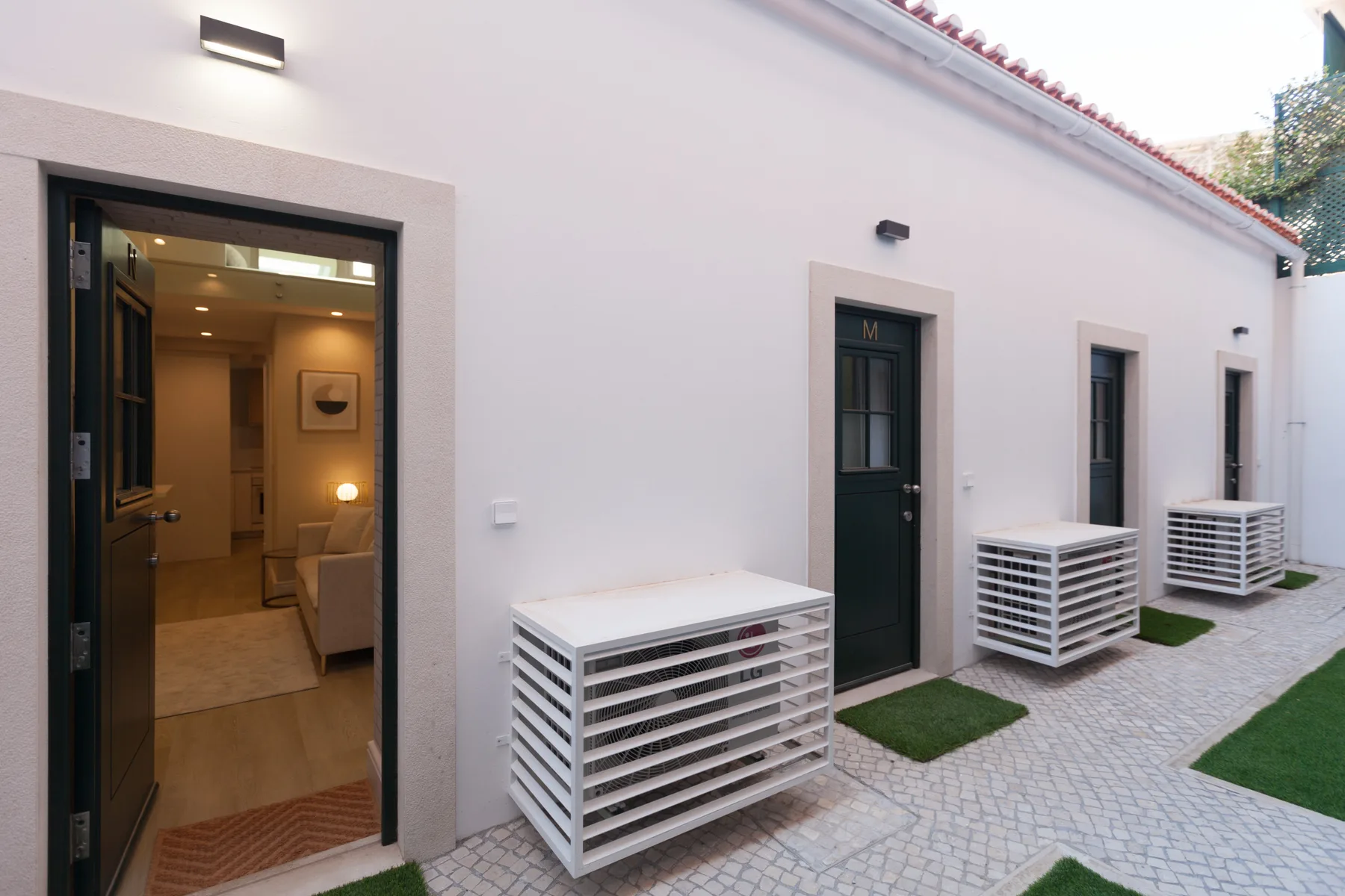 An exterior walkway with several dark doors, ventilation units, and an open doorway into a room.