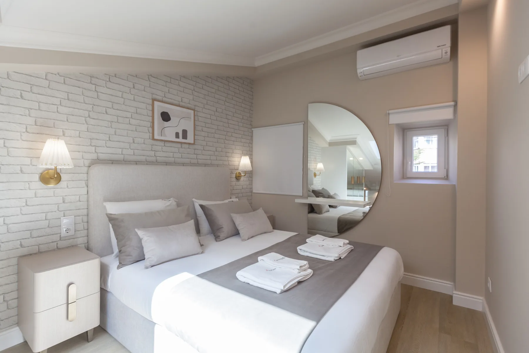 A bedroom with a neatly made bed and a round wall mirror.