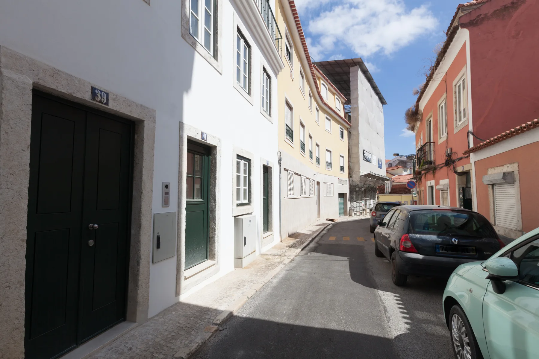 A narrow residential street lined with buildings and parked cars.