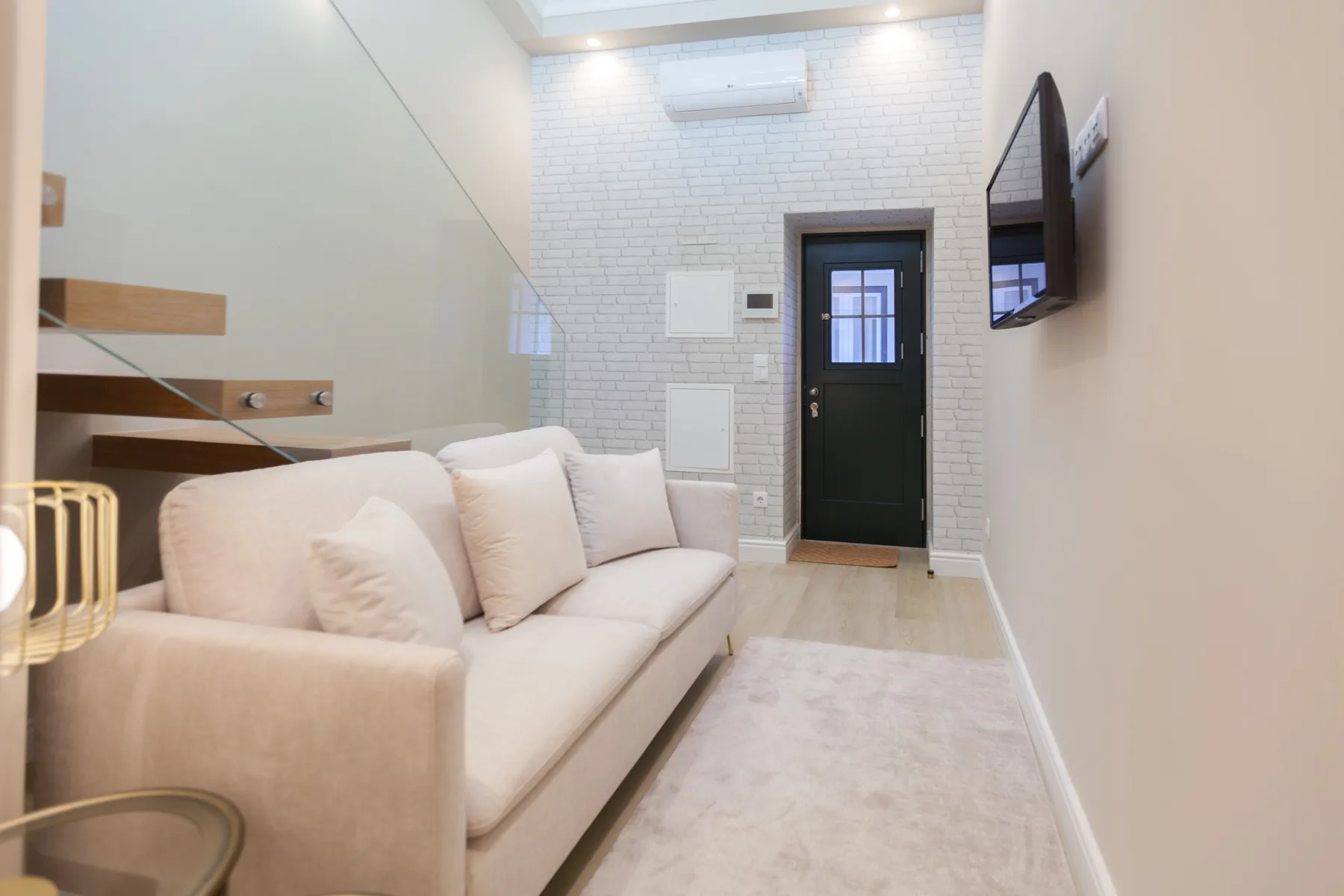A bright living room with a light-colored sofa and a wall-mounted television.