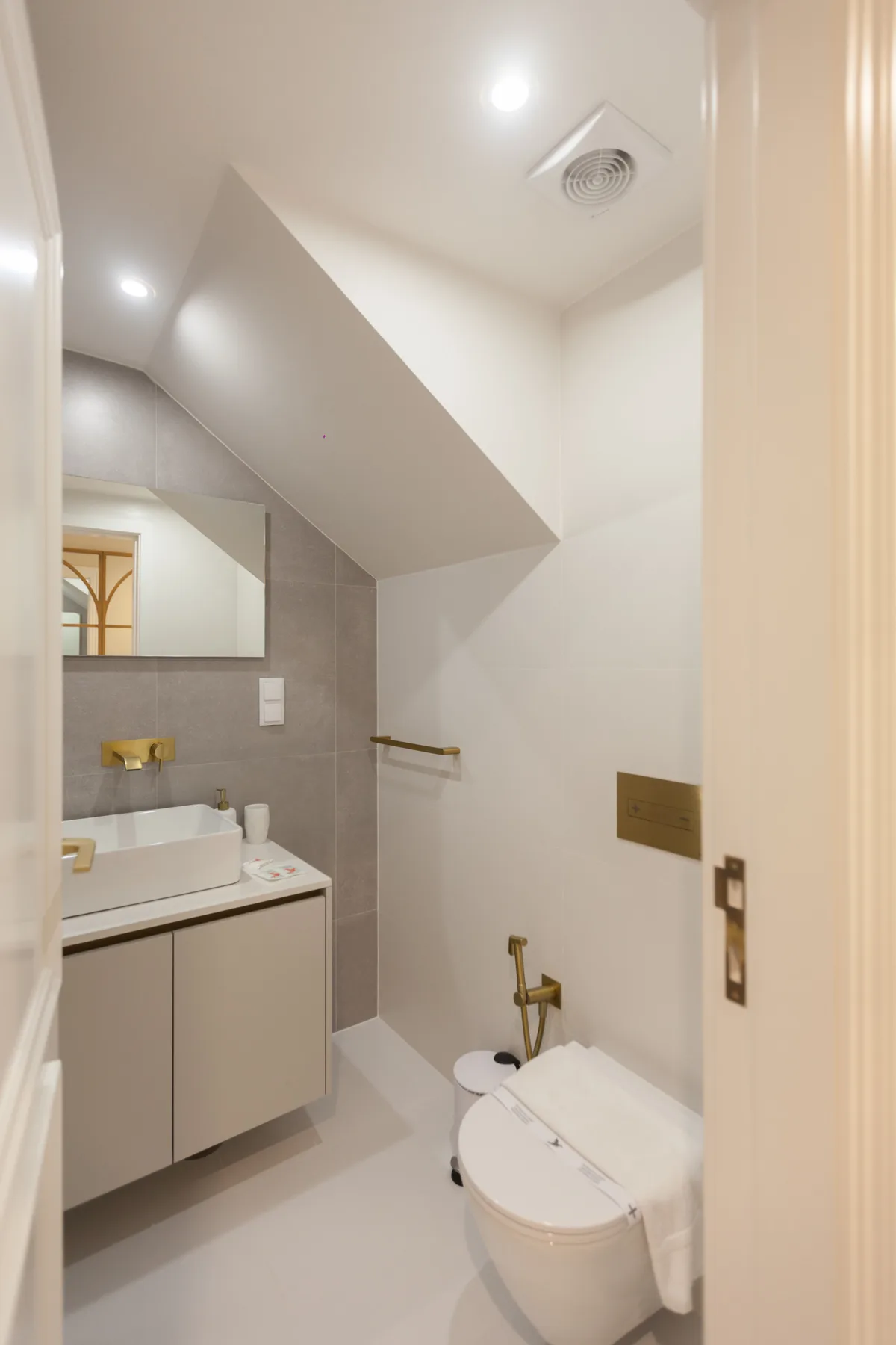 A compact bathroom with a vanity, mirror, and toilet beneath a sloped ceiling.