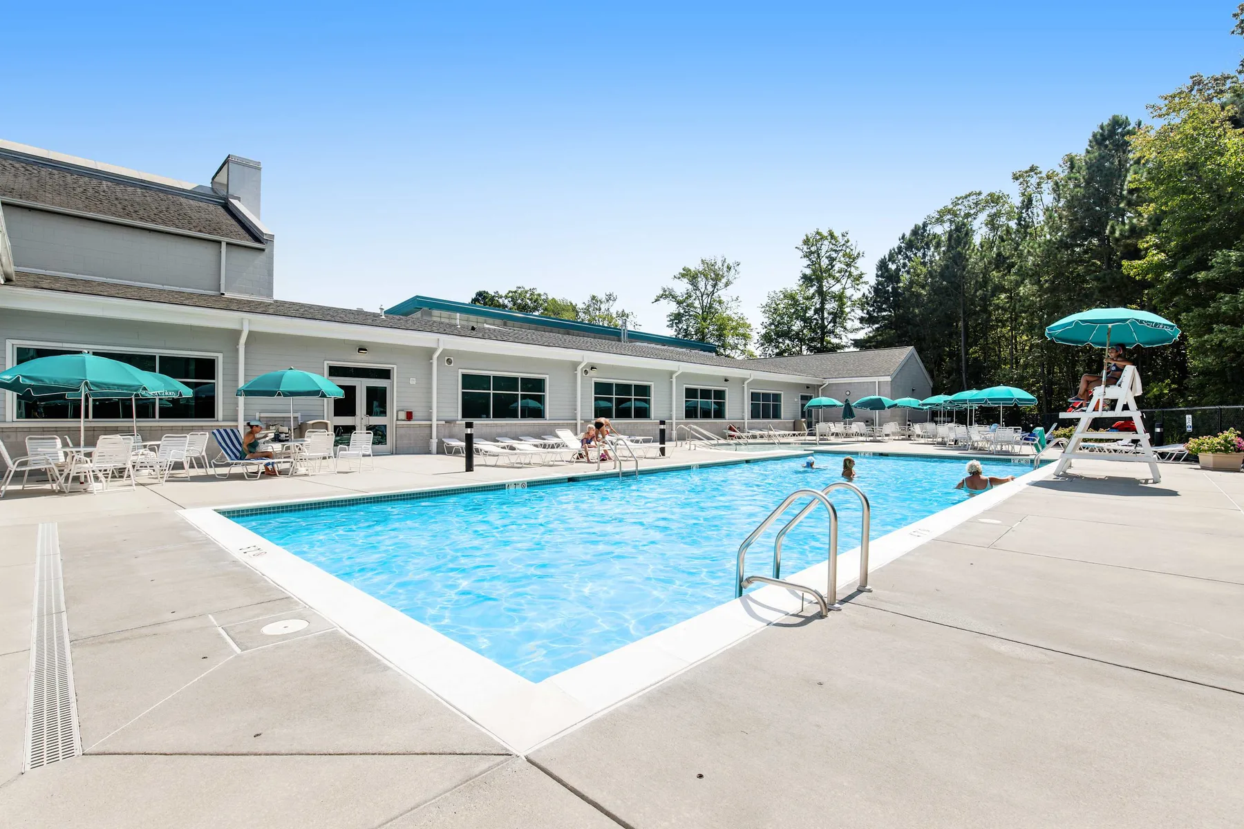 An outdoor swimming pool beside a low building, with umbrellas around the deck.