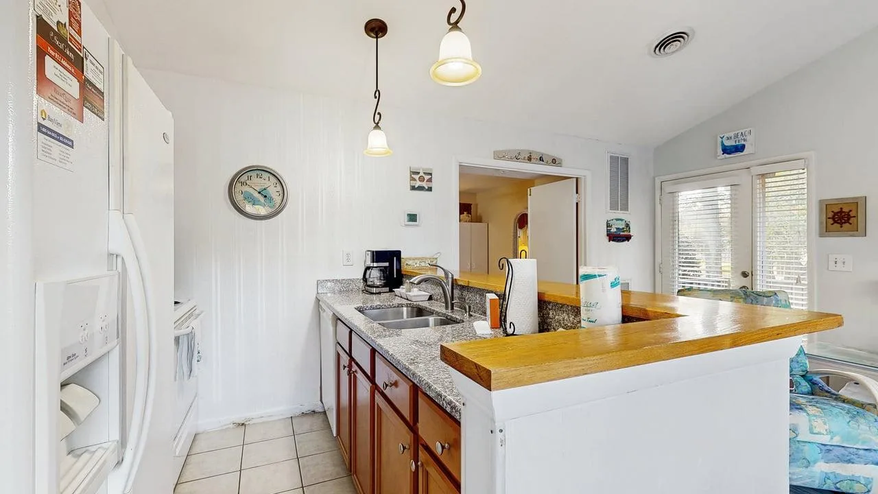 A bright kitchen with a long wooden counter and windows with blinds.