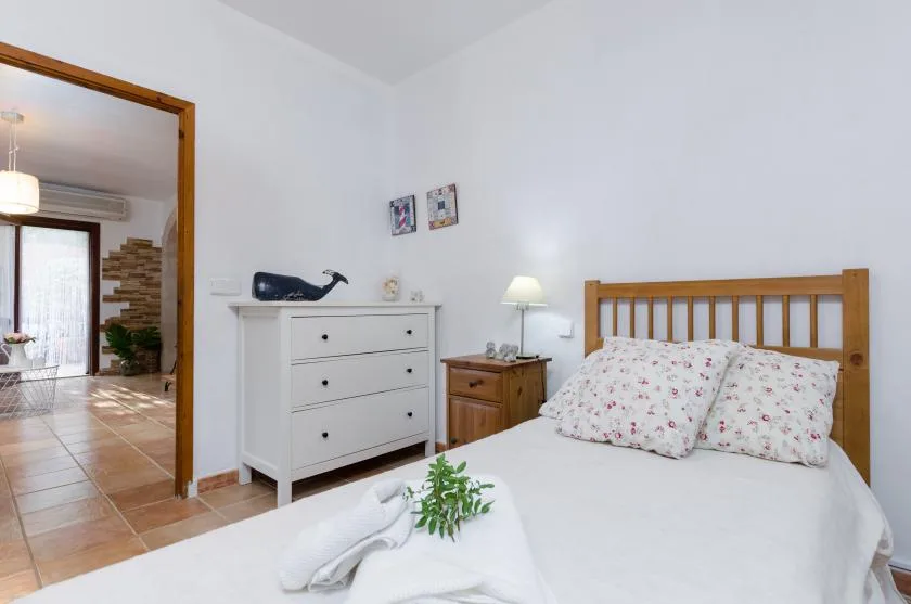 A bright bedroom with a wooden bed, white dresser, and bedside table.