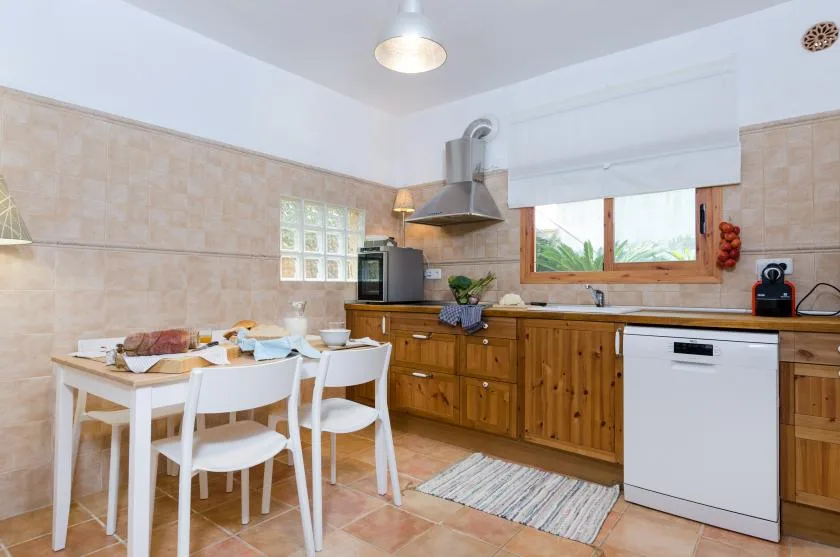 A tiled kitchen with wooden cabinets, a dining table, and a window.