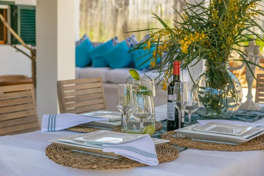 A dining table is set with plates, glassware, and a vase of yellow flowers.