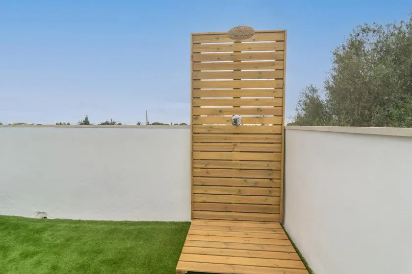 An outdoor shower with a wooden slatted screen stands beside a grassy area.