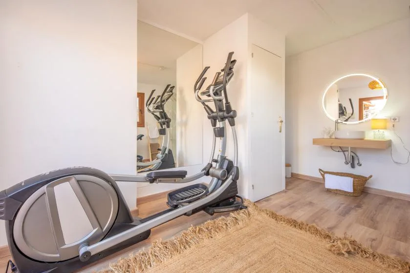 A bright fitness room with exercise equipment, a wall mirror, and a floating sink.