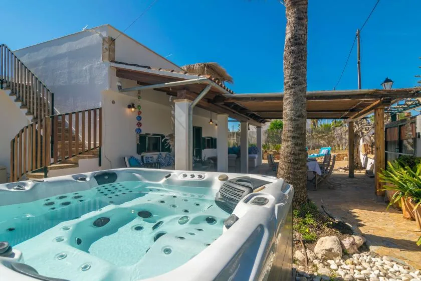 An outdoor hot tub sits beside a white building under a shaded pergola.