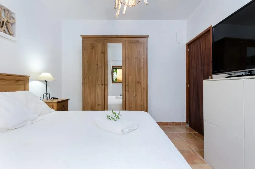 A bedroom with a neatly made bed, wooden wardrobe, and television.