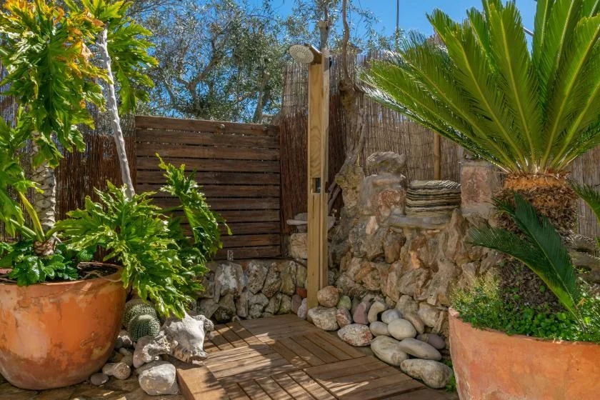 A garden entrance with a wooden gate, stone walls, and potted plants.
