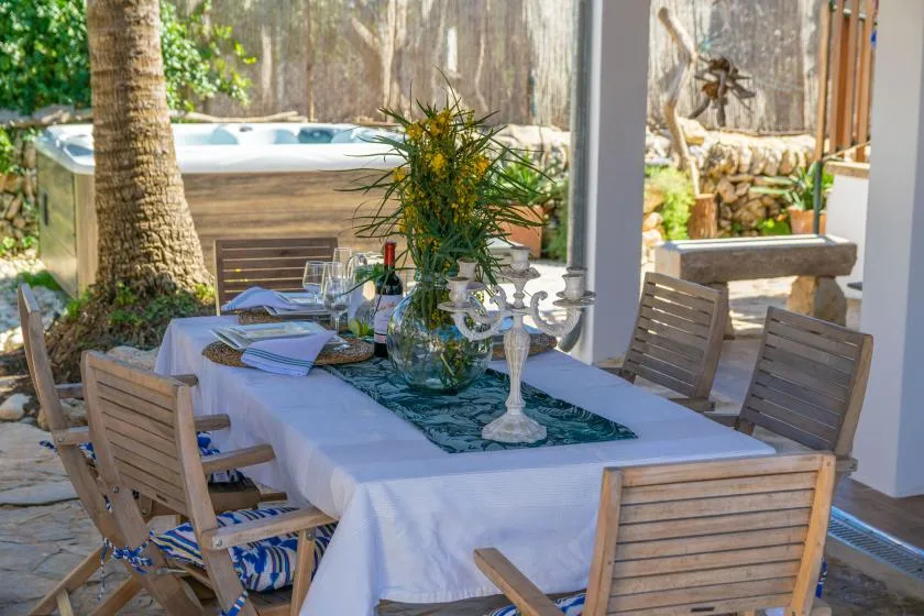 An outdoor dining table is set with plates and glassware beside a garden.