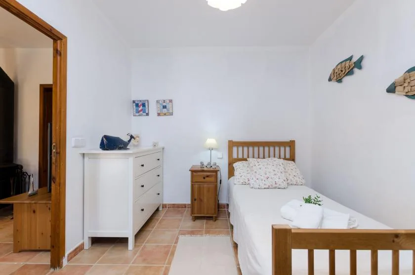 A bright bedroom with a single bed, wooden bedside table, and white dresser.