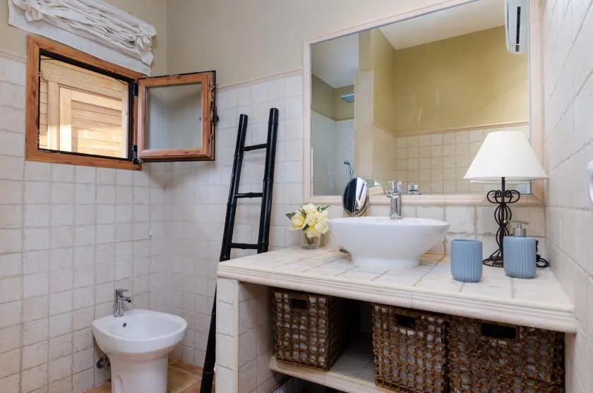 A tiled bathroom with a wide sink counter, mirror, and open window.
