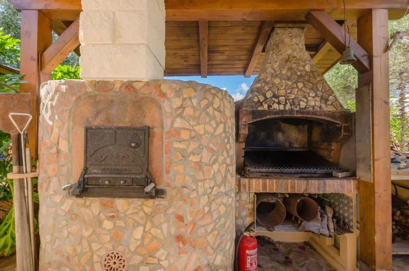 An outdoor stone barbecue area sits beneath a wooden roof.