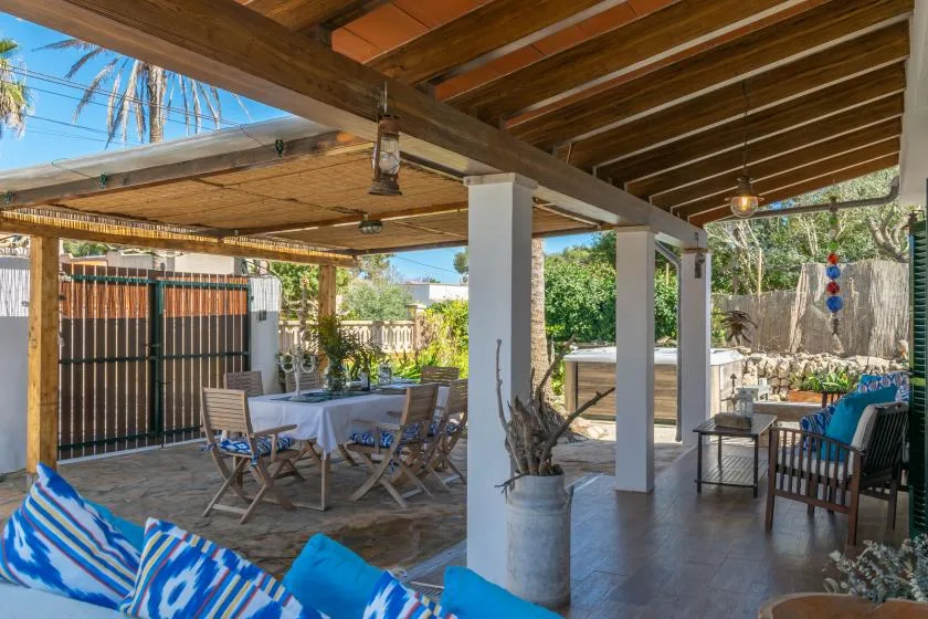 A covered outdoor patio with a dining table and seating beside a garden.