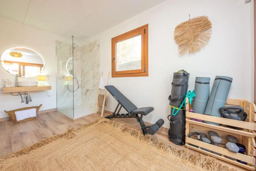 A bright exercise room with a workout bench and rolled mats beside a glass shower.