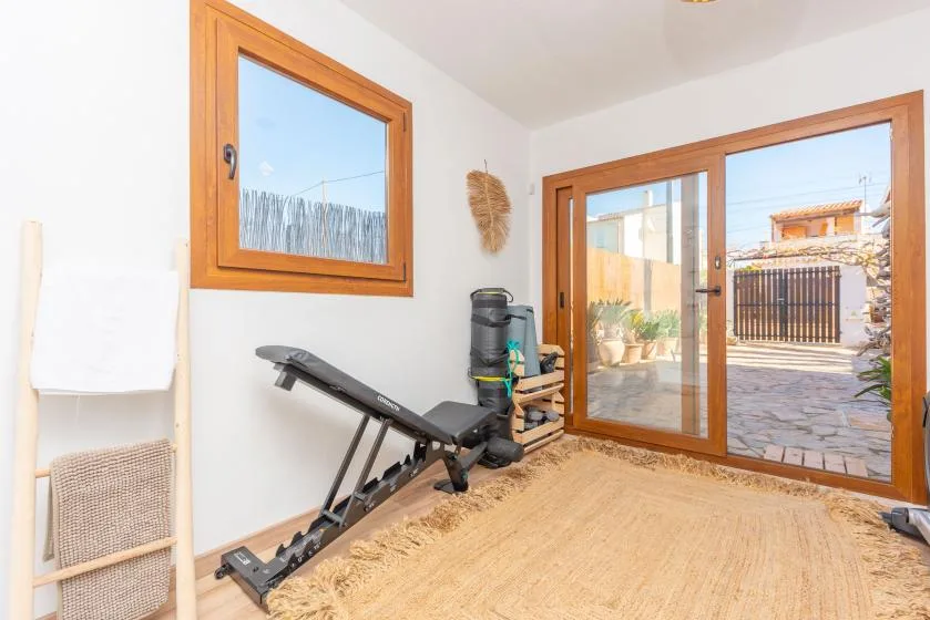 A bright room has exercise equipment beside glass doors opening onto a stone patio.