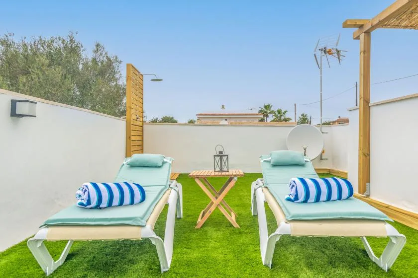 An outdoor lounging area with two sun loungers and a small table on green turf.