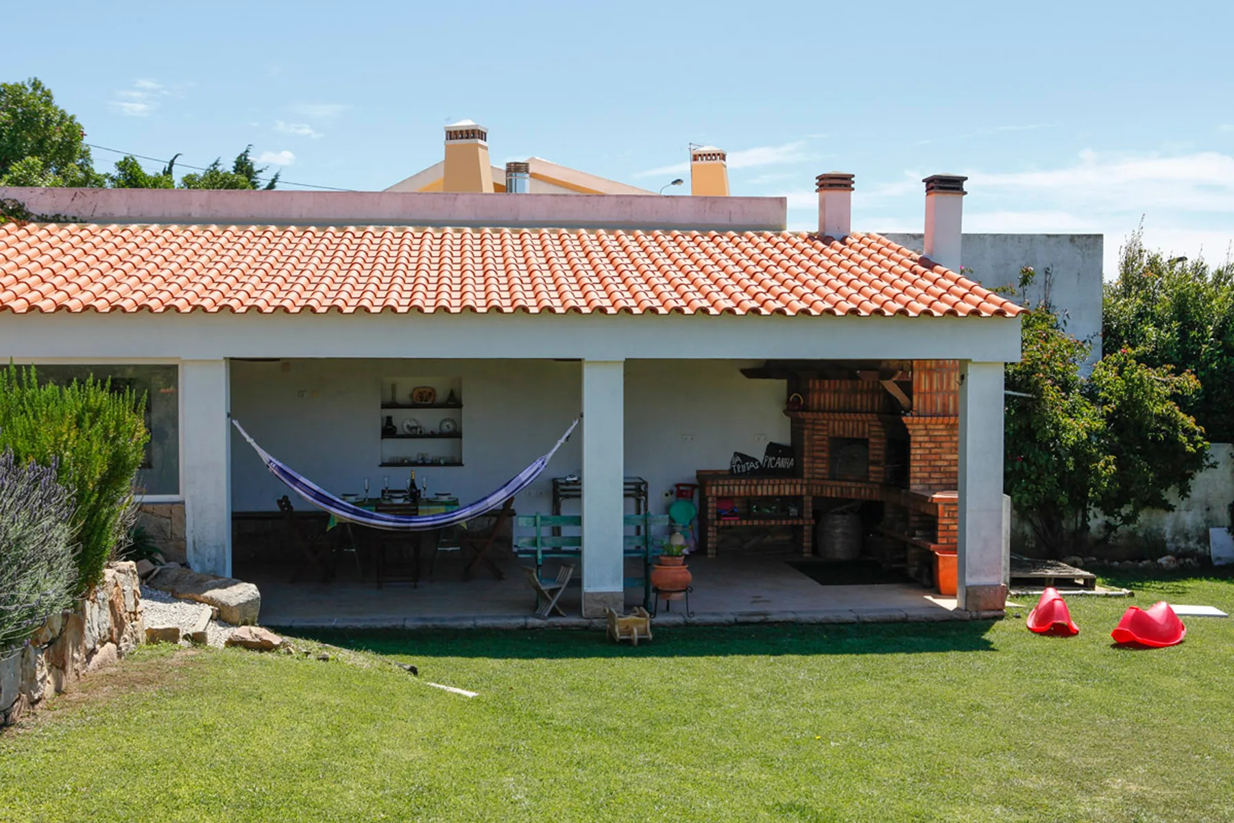A covered patio with a hammock, outdoor seating, and a brick barbecue.