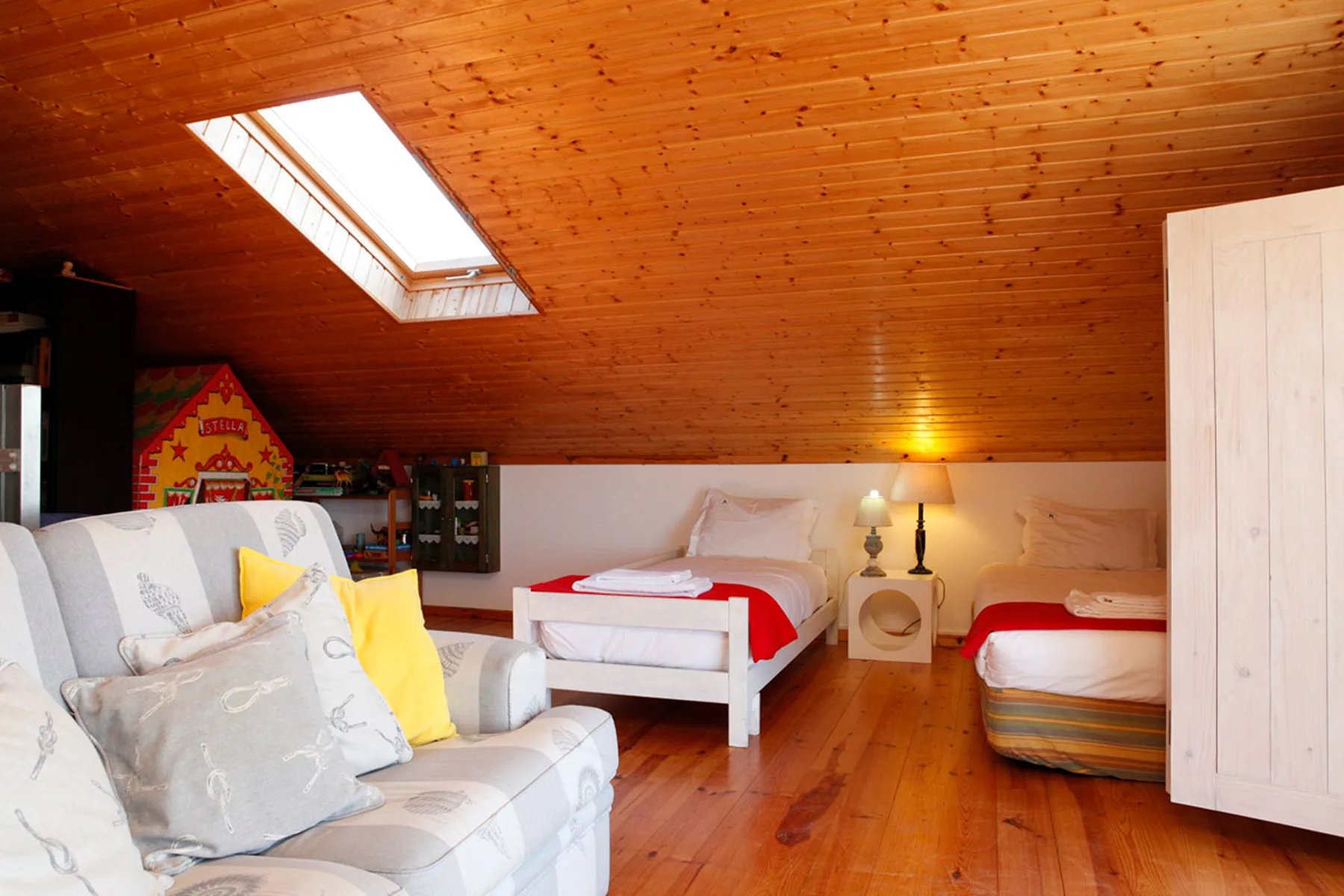 A wood-paneled attic bedroom with beds, seating, and a skylight.