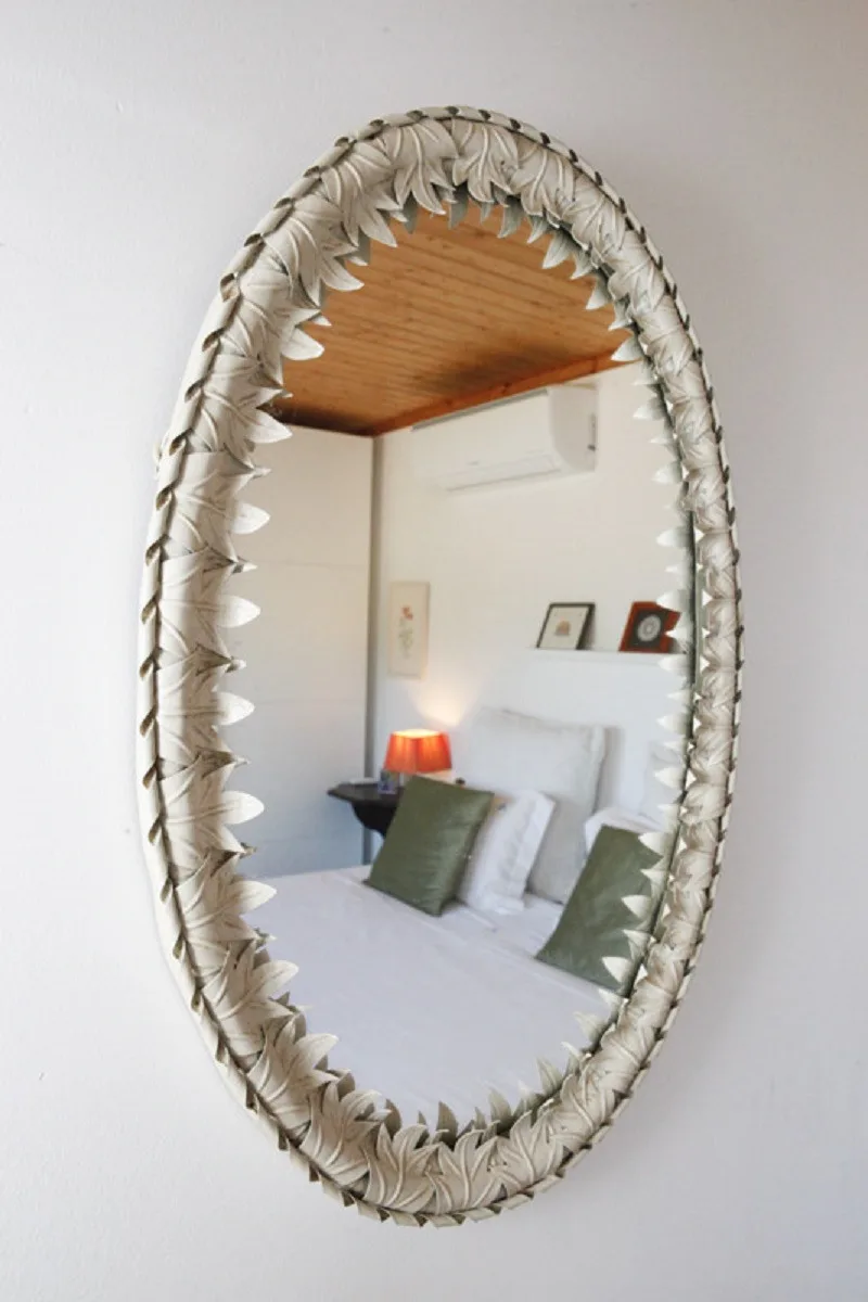 A bedroom reflected in an oval mirror, with a bed and bedside lamp.