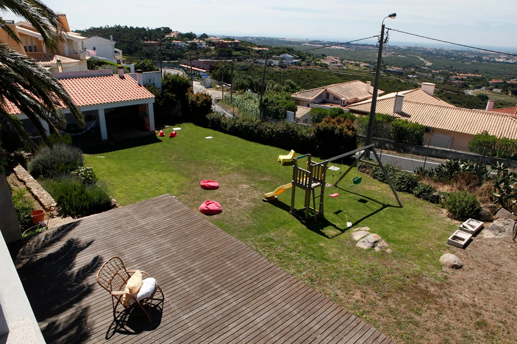 A garden with a wooden deck, lawn, and children’s play equipment overlooks the surrounding hillside.
