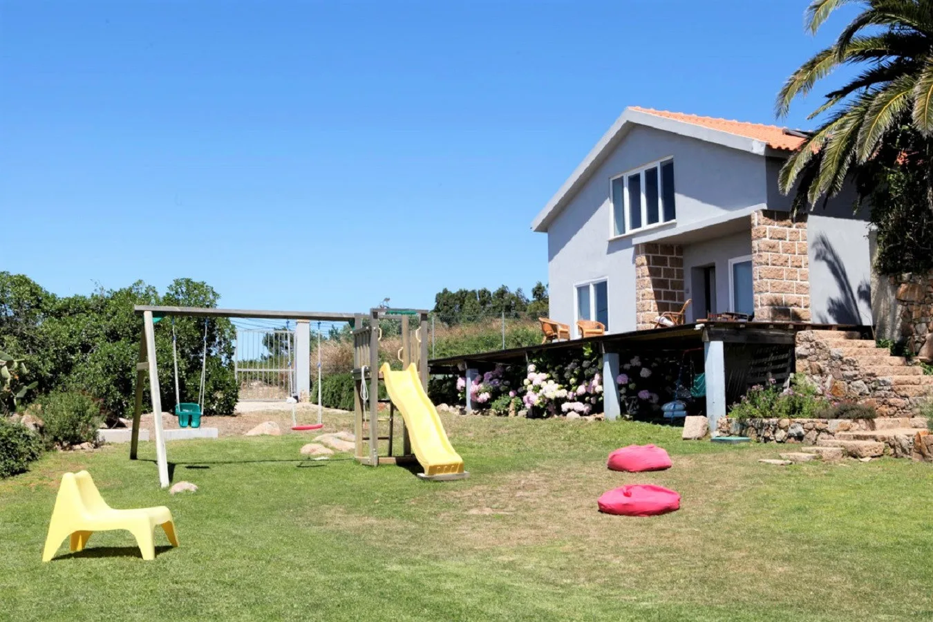 A house and garden with a lawn, swings, and a yellow slide.