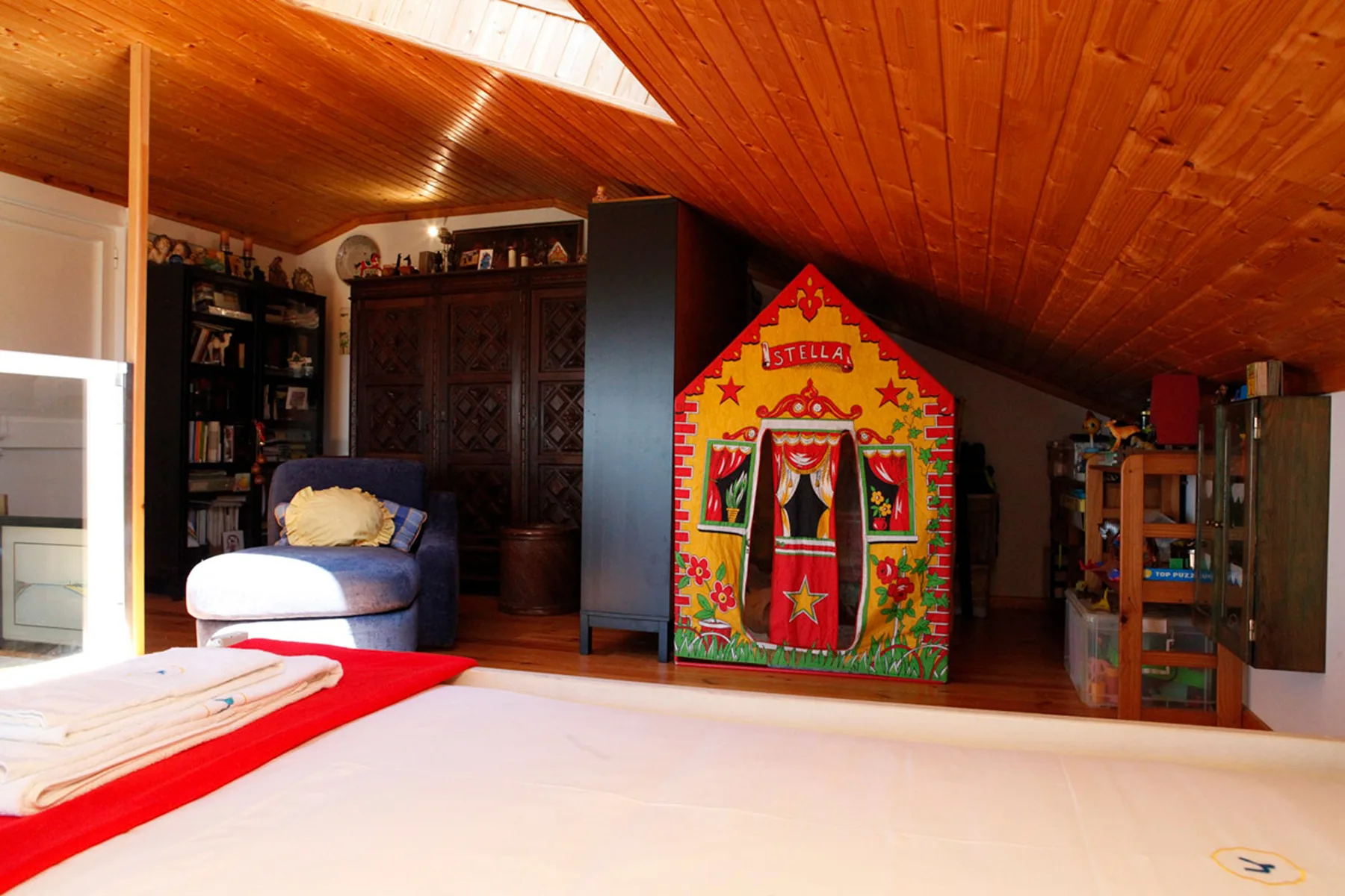 A bedroom with a colorful painted cabinet, a bed, and a wooden sloped ceiling.