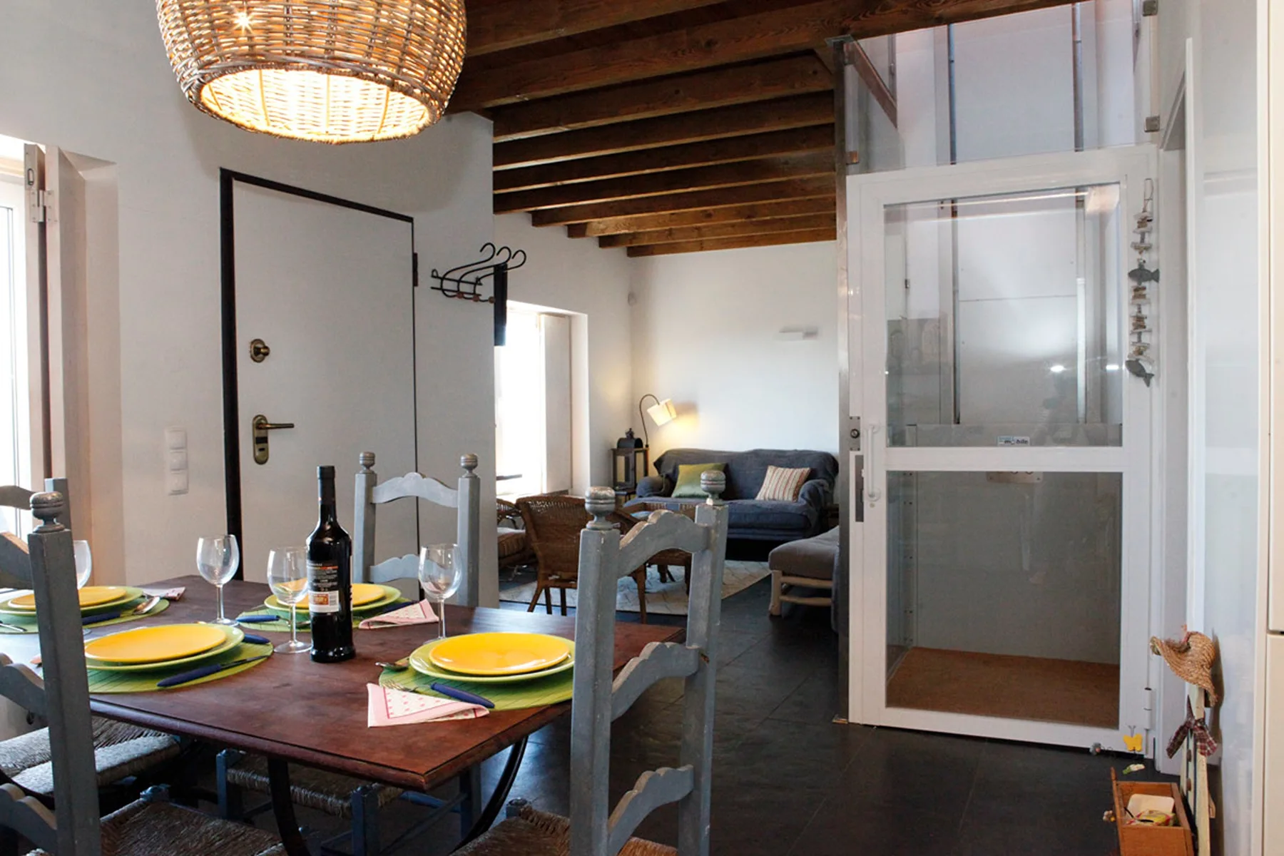 A dining area opens onto a living room with seating beneath exposed wooden beams.