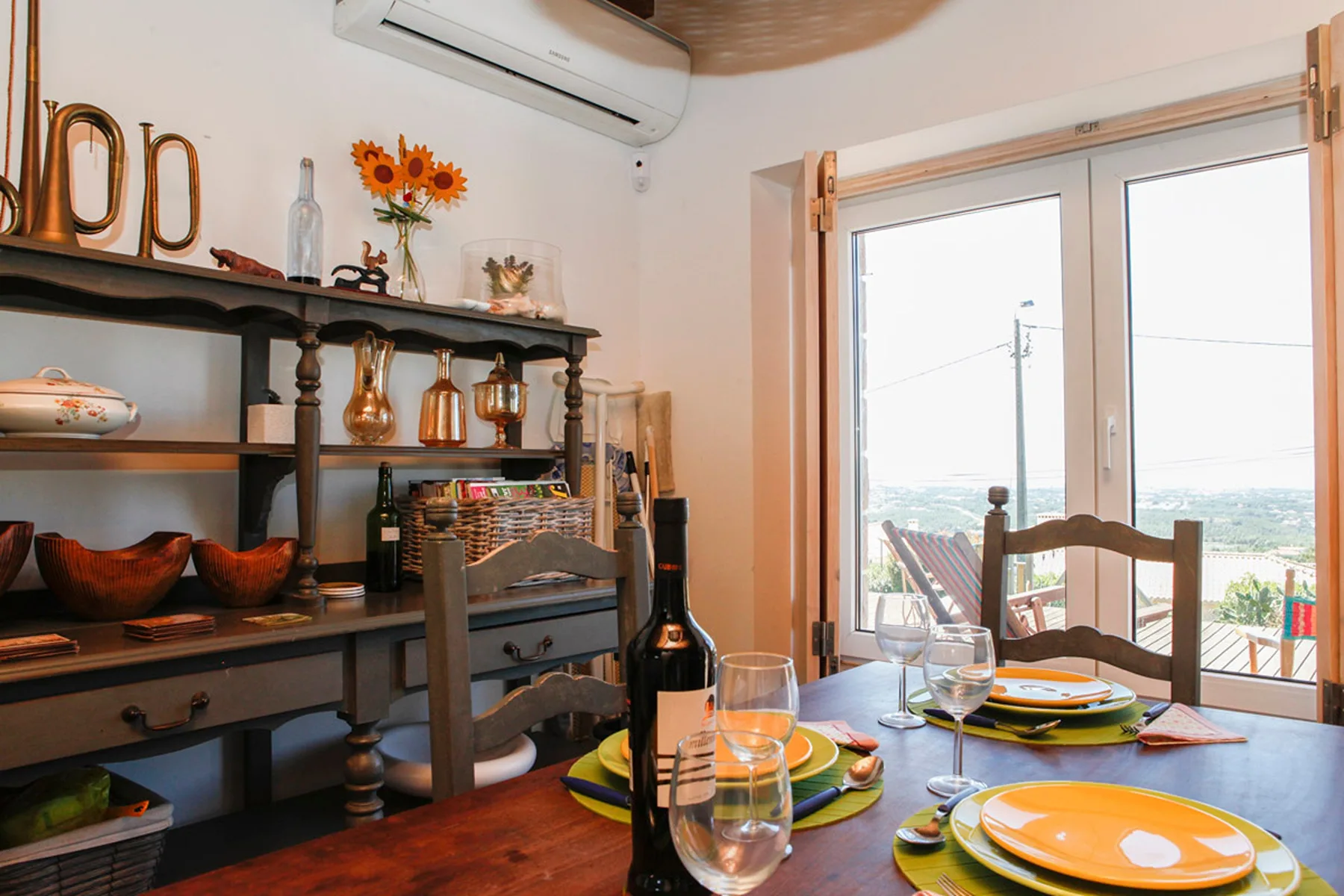 A dining area with a set table beside large windows overlooking the coast.