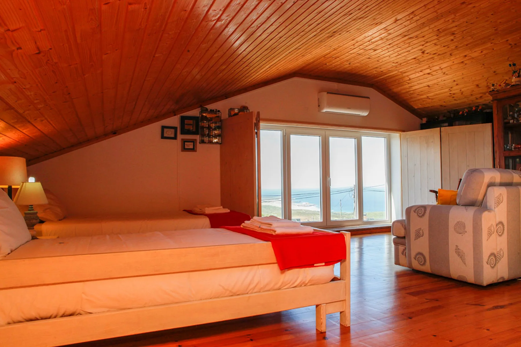 A bedroom with a sloped wooden ceiling and windows overlooking the sea.