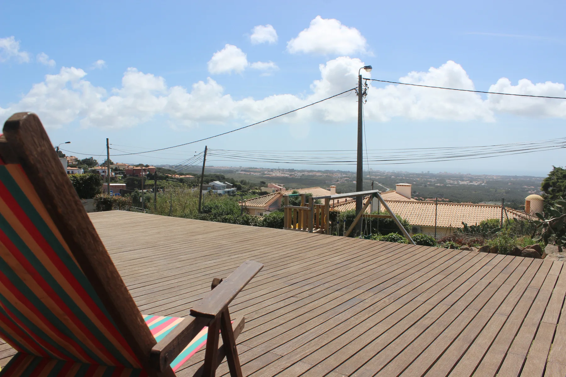 A wooden deck overlooks rooftops and a distant landscape beneath a blue sky.