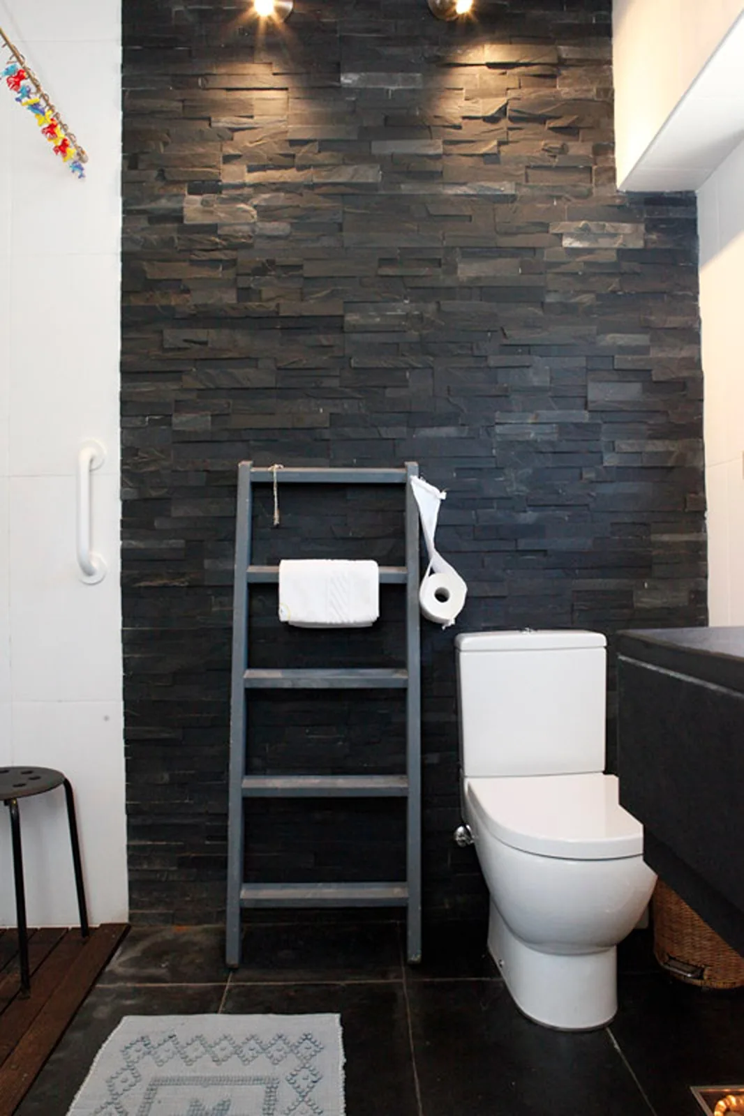 A bathroom with a toilet, towel rack, and dark tiled wall.