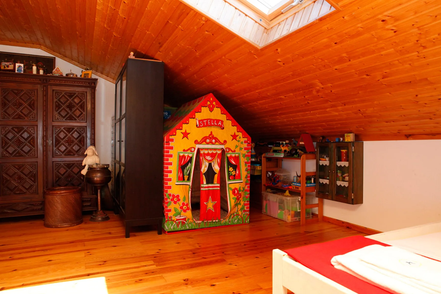 A bedroom with a colorful playhouse and storage cabinets beneath a sloped wooden ceiling.